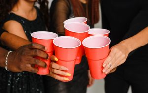 Waist up of six friends having fun and drinking alcohol during New Year party, isolated on white background. A group of cheerful friends of different nationalities clink glasses with red glasses at a party in the studio.